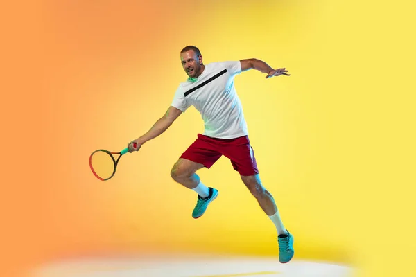Hombre caucásico deportista profesional jugando al tenis en el fondo del estudio en luz de neón — Foto de Stock