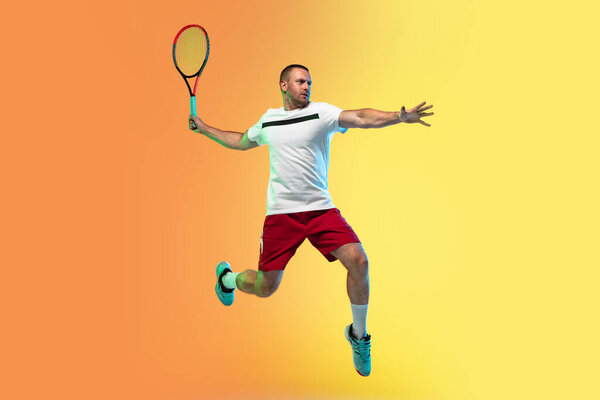 Caucasian male professional sportsman playing tennis on studio background in neon light