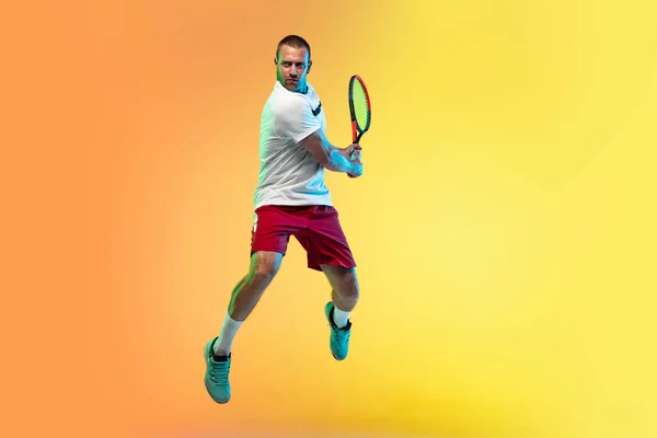 Kaukasischer männlicher Profisportler spielt Tennis auf Studiohintergrund im Neonlicht — Stockfoto