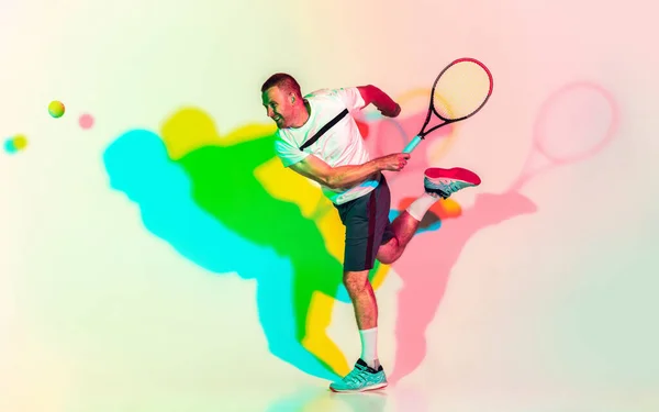 Кавказький професійний спортсмен грає в теніс на задньому плані студії в неоновому світлі — стокове фото