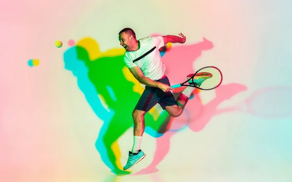 백인 남자 프로 운동 선수, 네온 빛으로 스튜디오 배경에서 테니스를 치는 모습 — 스톡 사진