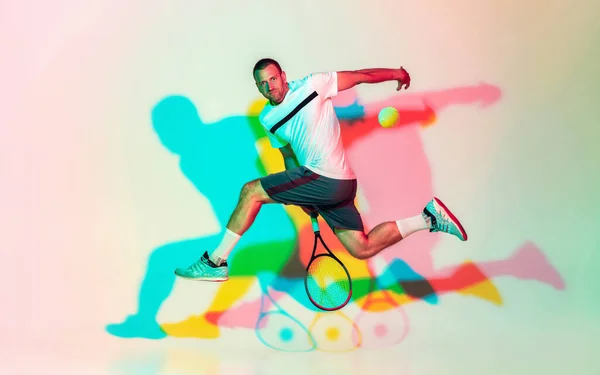 Hombre caucásico deportista profesional jugando al tenis en el fondo del estudio en luz de neón — Foto de Stock