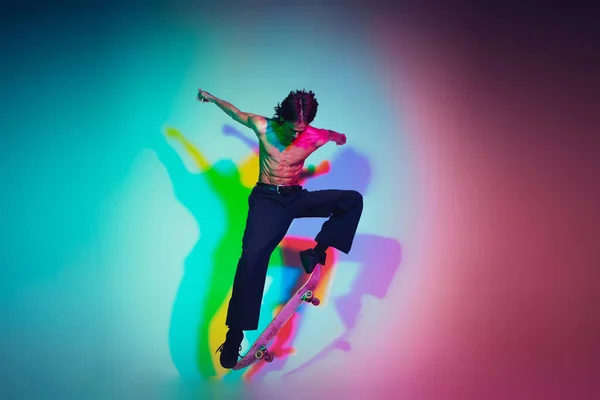 Skateboarder doet een truc geïsoleerd op studio achtergrond in kleurrijke neon licht — Stockfoto