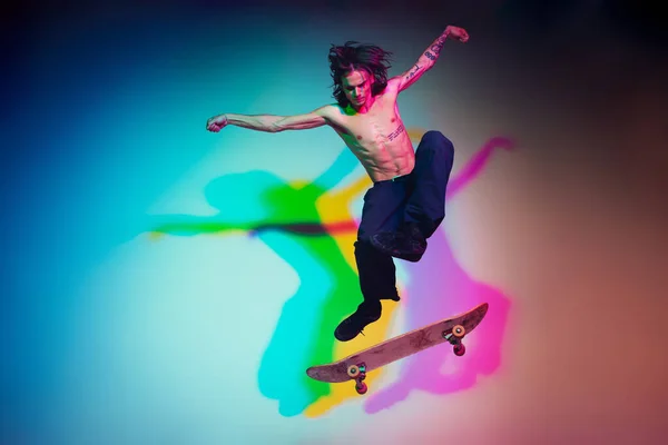 Скейтбордист выполняет трюк на фоне студии в цветном неоновом свете — стоковое фото