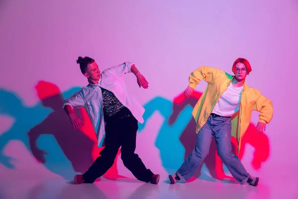 Joven hombre y mujer bailando hip-hop, estilo calle aislado en el fondo del estudio en luz de neón — Foto de Stock