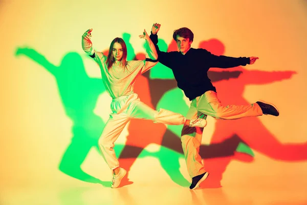 Young man and woman dancing hip-hop, street style isolated on studio background in neon light — Stock Photo, Image