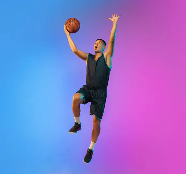 Jonge basketbalspeler in beweging op gradiënt studio achtergrond in neon licht — Stockfoto