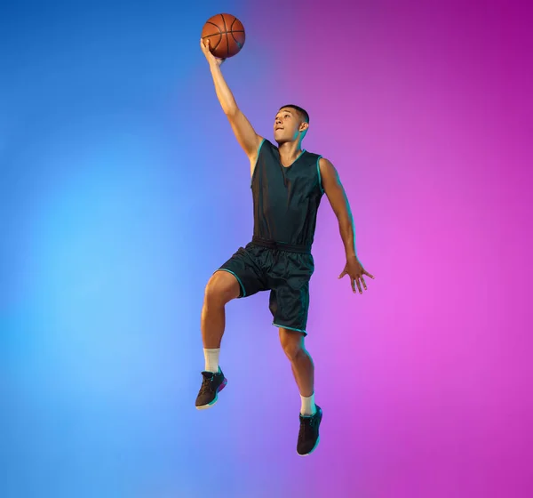 Joven jugador de baloncesto en movimiento en gradiente fondo del estudio en luz de neón —  Fotos de Stock