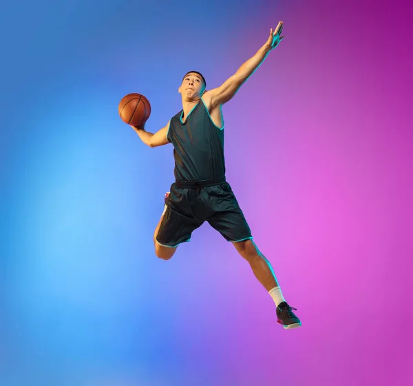 Młody koszykarz w ruchu na tle gradientowego studia w neonowym świetle — Zdjęcie stockowe