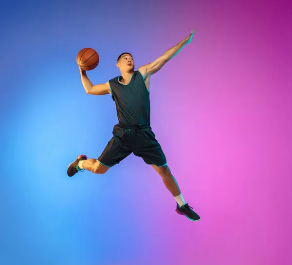 Joven jugador de baloncesto en movimiento en gradiente fondo del estudio en luz de neón — Foto de Stock