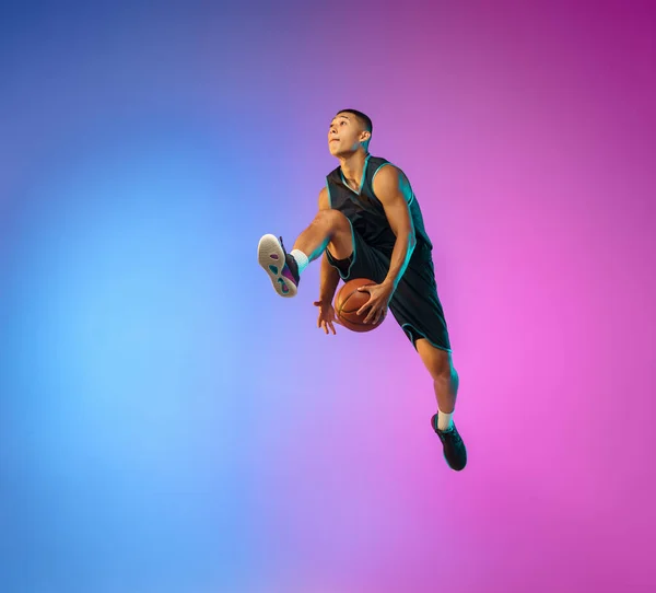 Молодий баскетболіст у русі на градієнтному студійному фоні в неоновому світлі — стокове фото