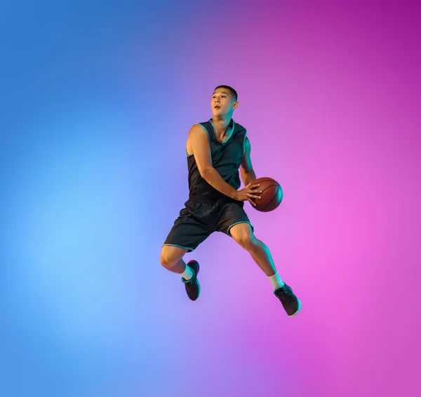 Jovem jogador de basquete em movimento no fundo do estúdio gradiente em luz de néon — Fotografia de Stock