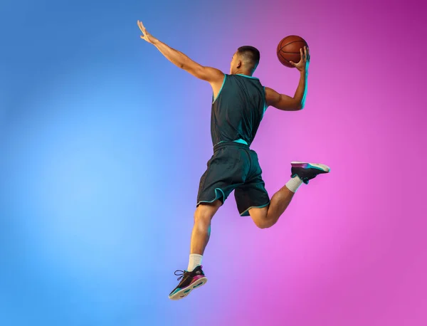 Joven jugador de baloncesto en movimiento en gradiente fondo del estudio en luz de neón — Foto de Stock