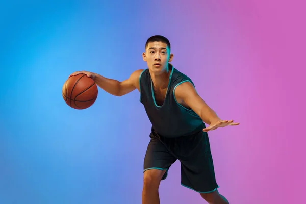 Joven jugador de baloncesto en movimiento en gradiente fondo del estudio en luz de neón —  Fotos de Stock