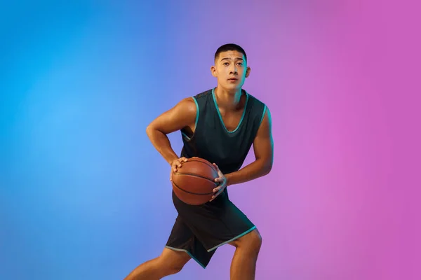 Joven jugador de baloncesto en movimiento en gradiente fondo del estudio en luz de neón — Foto de Stock