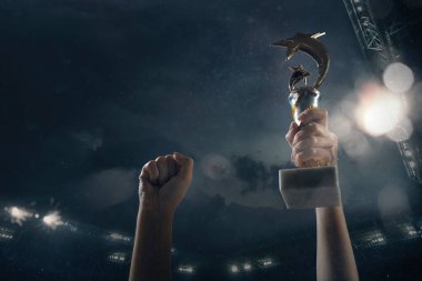 Galibiyet ödülü, erkek eli bulutlu gökyüzüne karşı kazananların kupasını sıkıyor.