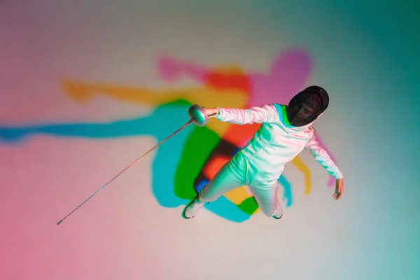 Adolescente en costume d'escrime avec épée à la main sur fond dégradé avec lumière au néon, vue de dessus — Photo