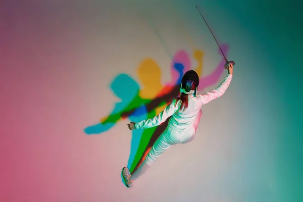 Adolescente en costume d'escrime avec épée à la main sur fond dégradé avec lumière au néon, vue de dessus — Photo