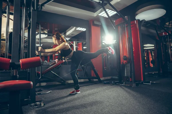 Junge muskulöse Kaukasierin, die im Fitnessstudio mit Geräten übt. Wellness, gesunder Lebensstil, Bodybuilding. — Stockfoto
