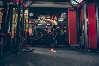Genç kaslı beyaz kadın spor salonunda aletlerle pratik yapıyor. Sağlık, sağlıklı yaşam tarzı, vücut geliştirme..