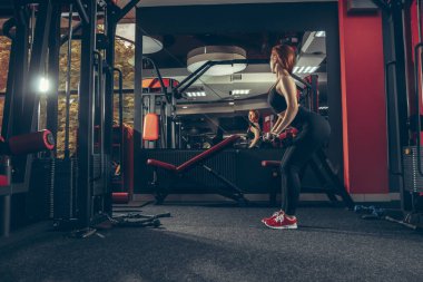 Genç kaslı beyaz kadın spor salonunda aletlerle pratik yapıyor. Sağlık, sağlıklı yaşam tarzı, vücut geliştirme..