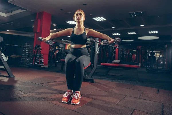 Junge muskulöse Kaukasierin, die im Fitnessstudio mit Geräten übt. Wellness, gesunder Lebensstil, Bodybuilding. — Stockfoto