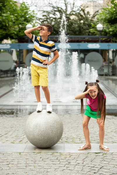 Dvě usměvavé děti, chlapec a dívka běží společně ve městě, město v letní den — Stock fotografie