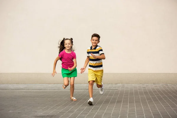Δύο χαμογελαστά παιδιά, αγόρι και κορίτσι τρέχουν μαζί στην πόλη, την καλοκαιρινή μέρα — Φωτογραφία Αρχείου