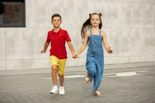 Deux enfants souriants, garçon et fille courant ensemble en ville, ville dans la journée d'été — Photo