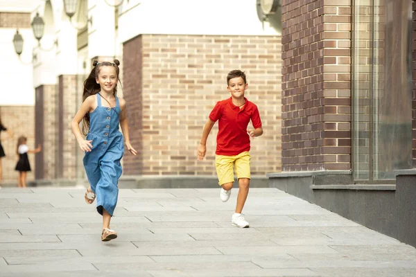 Двоє усміхнених дітей, хлопчик і дівчинка біжать разом у місті, місті в літній день — стокове фото