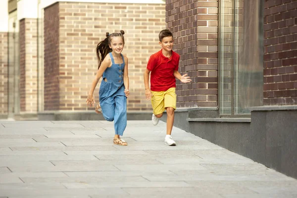 Deux enfants souriants, garçon et fille courant ensemble en ville, ville dans la journée d'été — Photo