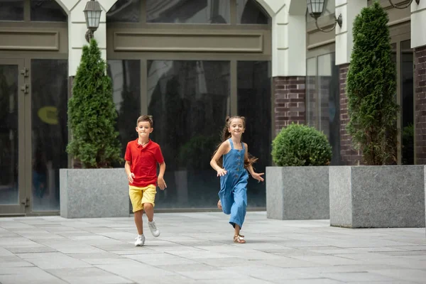 Två leende barn, pojke och flicka springer tillsammans i stan, stad på sommardagen — Stockfoto