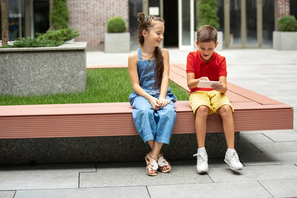 Dvě usměvavé děti, chlapec a dívka hrají smartphone společně ve městě, město v letní den — Stock fotografie