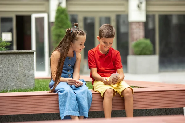 Duas crianças sorridentes, menino e menina jogando smartphone juntos na cidade, cidade no dia de verão — Fotografia de Stock