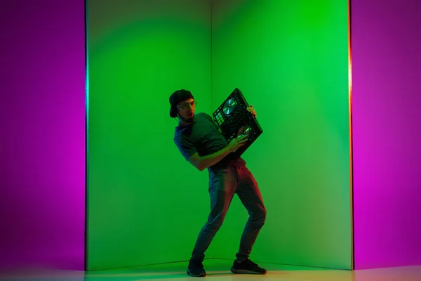 Jovem músico caucasiano em fones de ouvido realizando em fundo bicolor verde-roxo em luz de néon — Fotografia de Stock