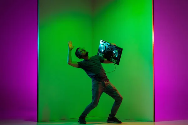 Ung kaukasiska musiker i hörlurar utför på tvåfärgad grön-lila bakgrund i neon ljus — Stockfoto