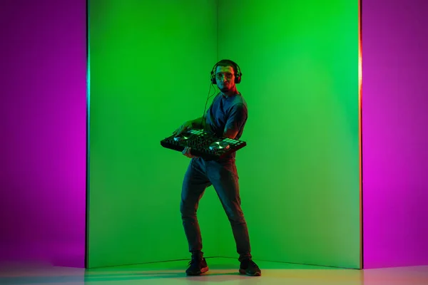 ネオン光の中で緑紫色の背景で演奏ヘッドフォンで若い白人音楽家 — ストック写真