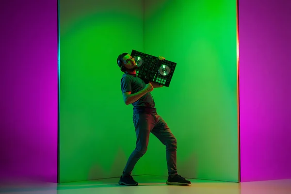 Jovem músico caucasiano em fones de ouvido realizando em fundo bicolor verde-roxo em luz de néon — Fotografia de Stock