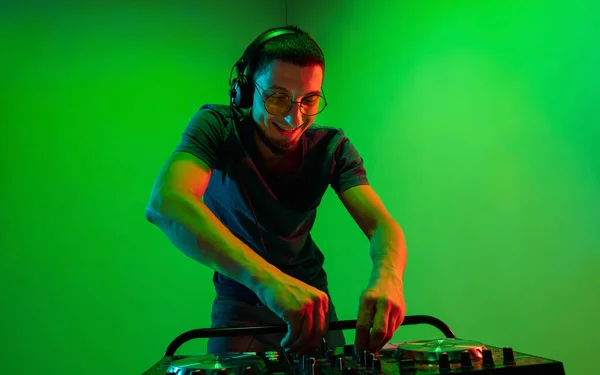 Junger kaukasischer Musiker mit Kopfhörern performt auf grünem Hintergrund im Neonlicht — Stockfoto