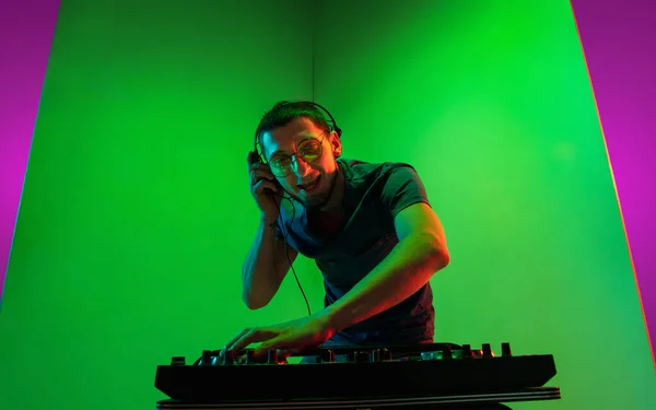 Joven músico caucásico en audífonos actuando sobre fondo bicolor verde-púrpura en luz de neón — Foto de Stock