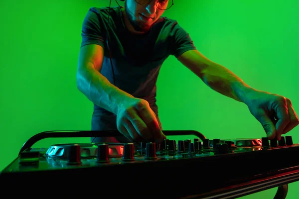 Ung kaukasisk musiker i hörlurar utför på grön bakgrund i neon ljus — Stockfoto
