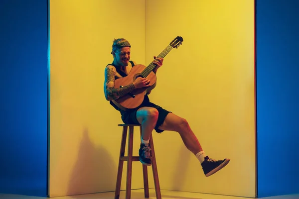 Ung kaukasisk musiker inspirerad utföra på gul bakgrund i neonljus — Stockfoto