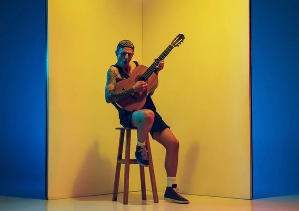 Junge kaukasische Musiker inspiriert, auf gelbem Hintergrund in Neonlicht aufzutreten — Stockfoto