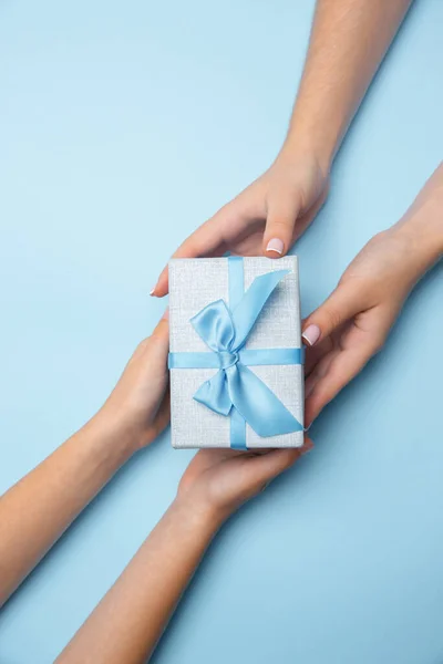 İnsanların elleri mavi arka planda izole edilmiş bir hediye, sürpriz bir kutu tutuyor. — Stok fotoğraf