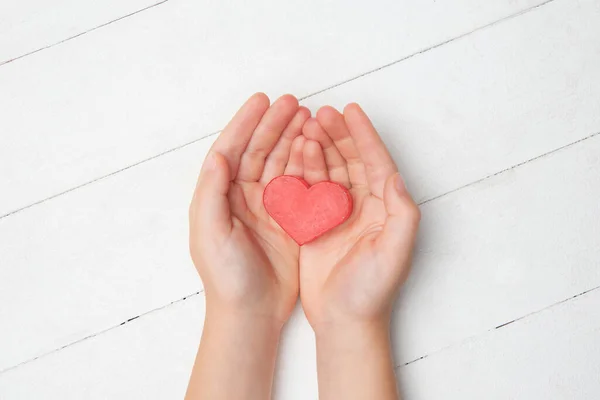 Human hands holding, giving heart isolated on white wooden background — Stock Photo, Image