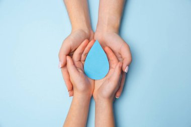 Beyaz ahşap zeminde izole edilmiş su damlasını tutan insan elleri