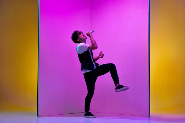 Ung manlig musiker, sångare som uppträder på rosa-orange bakgrund i neonljus — Stockfoto