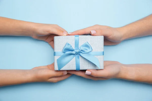 Manos humanas sosteniendo un regalo, regalo, caja sorpresa aislada sobre fondo azul — Foto de Stock