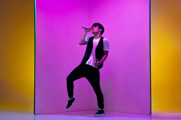 Jovem músico masculino, cantor realizando no fundo rosa-alaranjado em luz de néon — Fotografia de Stock