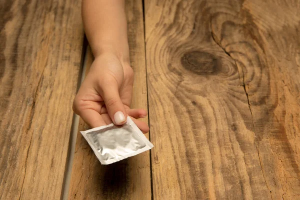 Kvinna hand innehav kondom isolerad på trä bakgrund — Stockfoto